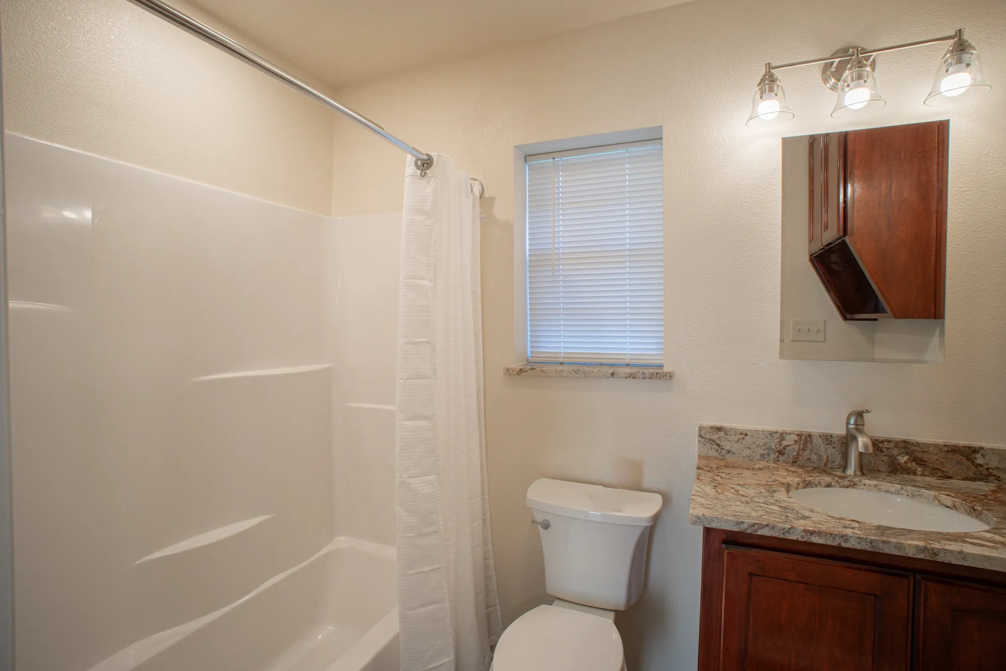Bathroom featuring a white tub/shower combination, a vanity with a stone countertop, a circular basin, and a chrome faucet