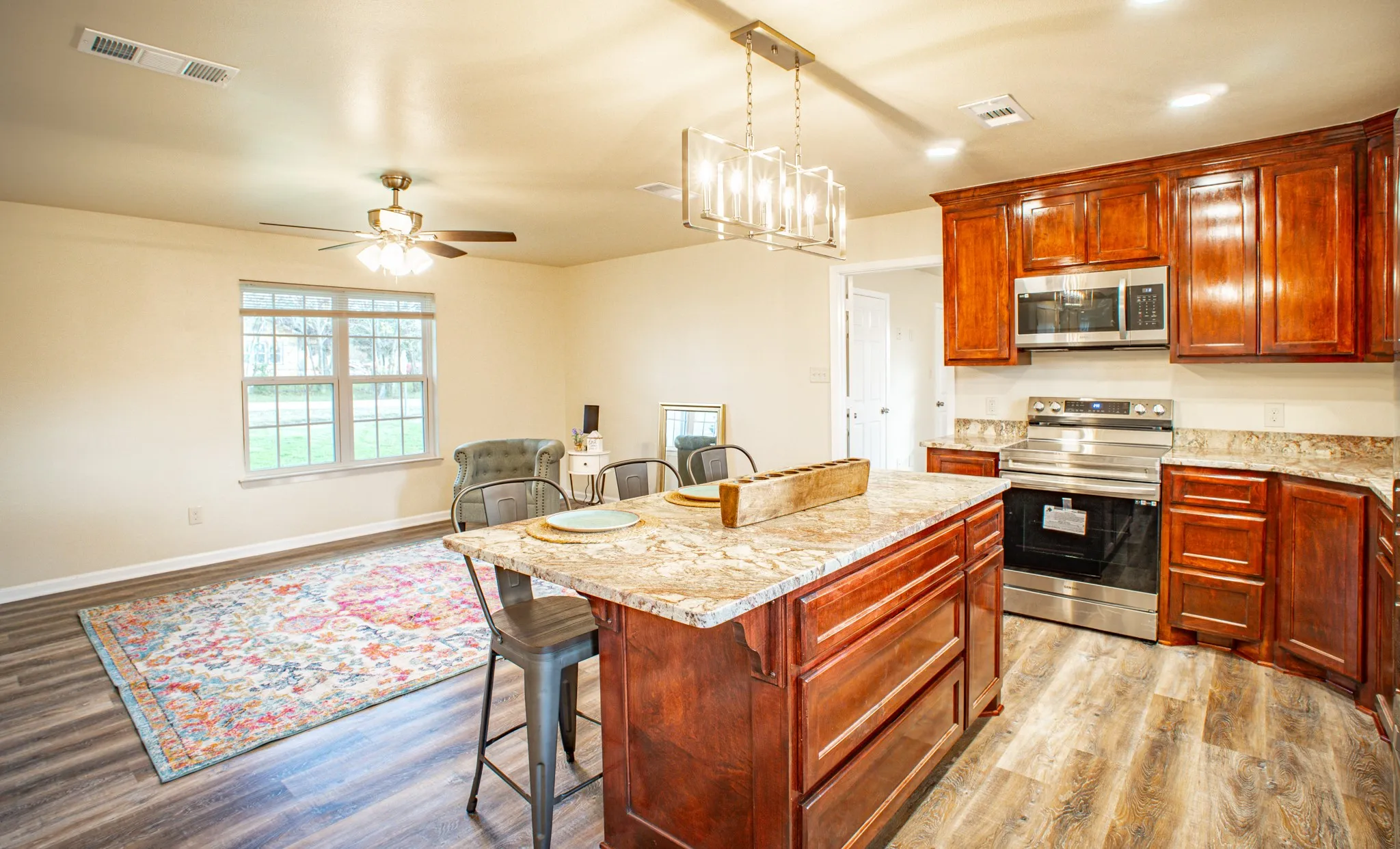 Open-concept kitchen featuring an island with a light-toned countertop, rich wood-finish cabinetry, stainless steel appliances, and wood-finish flooring