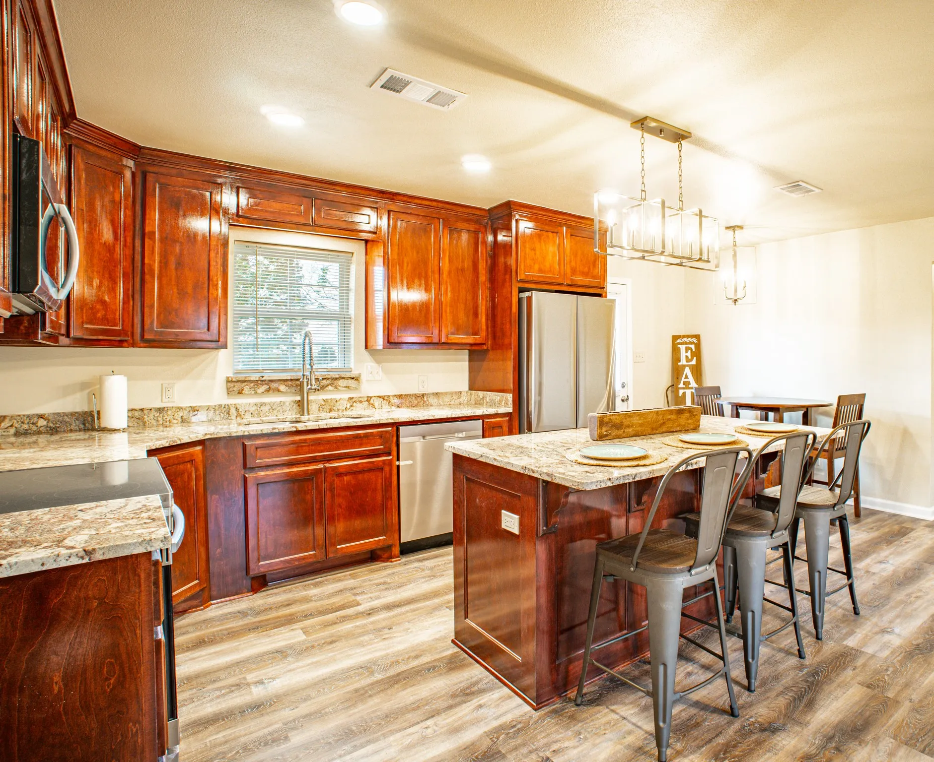 Kitchen featuring wood cabinetry, light-toned granite countertops, stainless steel appliances, a center island with seating, and wood-finish flooring