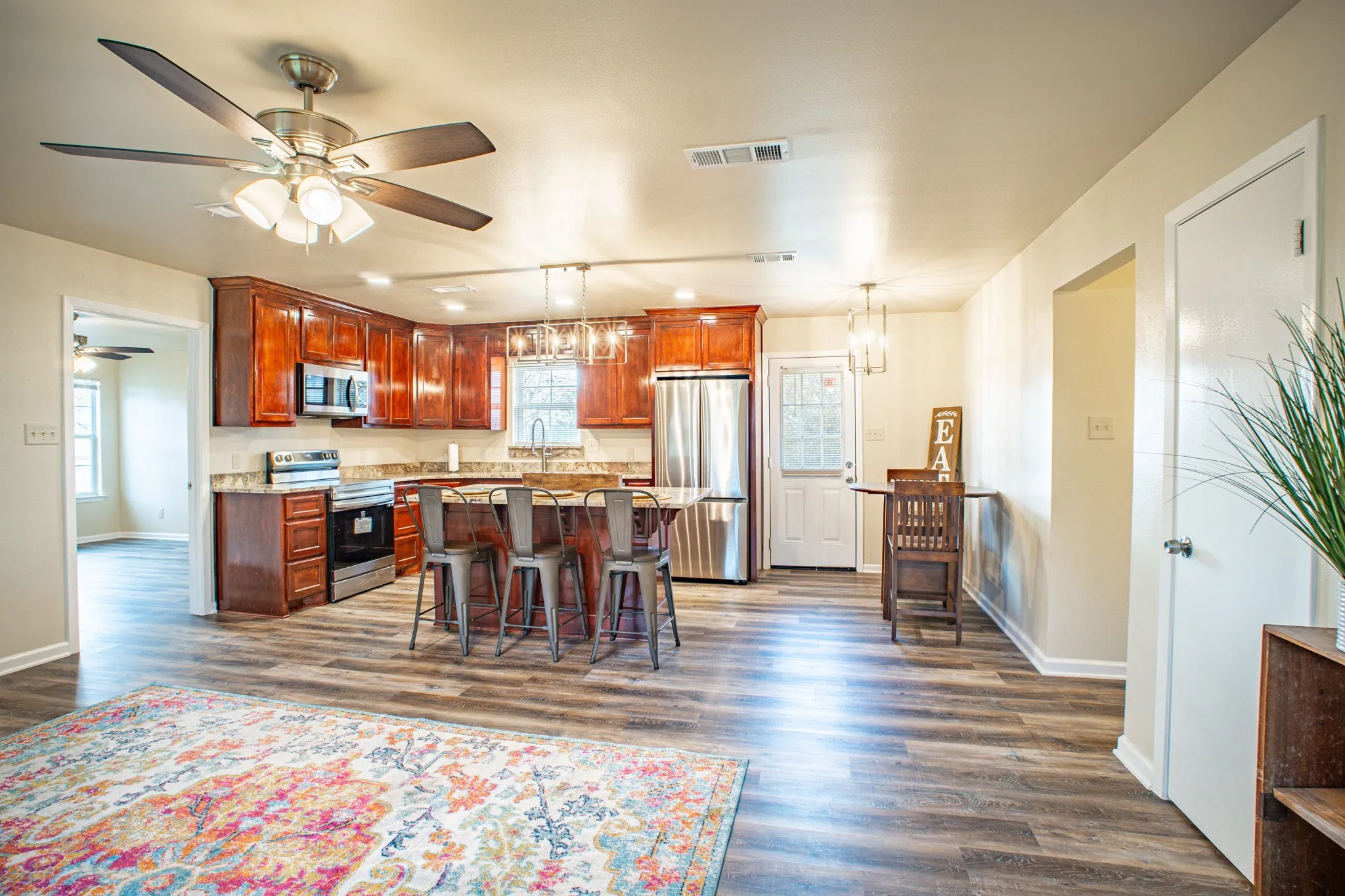 Open-concept kitchen and living area featuring wood-finish flooring, warm-toned cabinetry, stainless steel appliances, and an island with seating