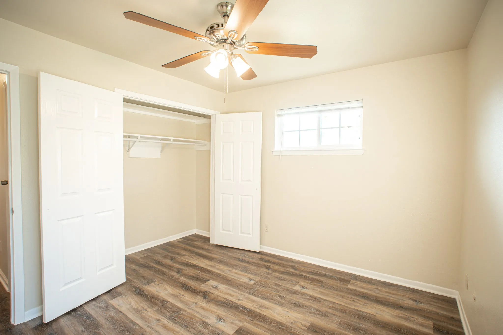 Room featuring wood-finish flooring, a ceiling fan with light fixture, and a window with white trim