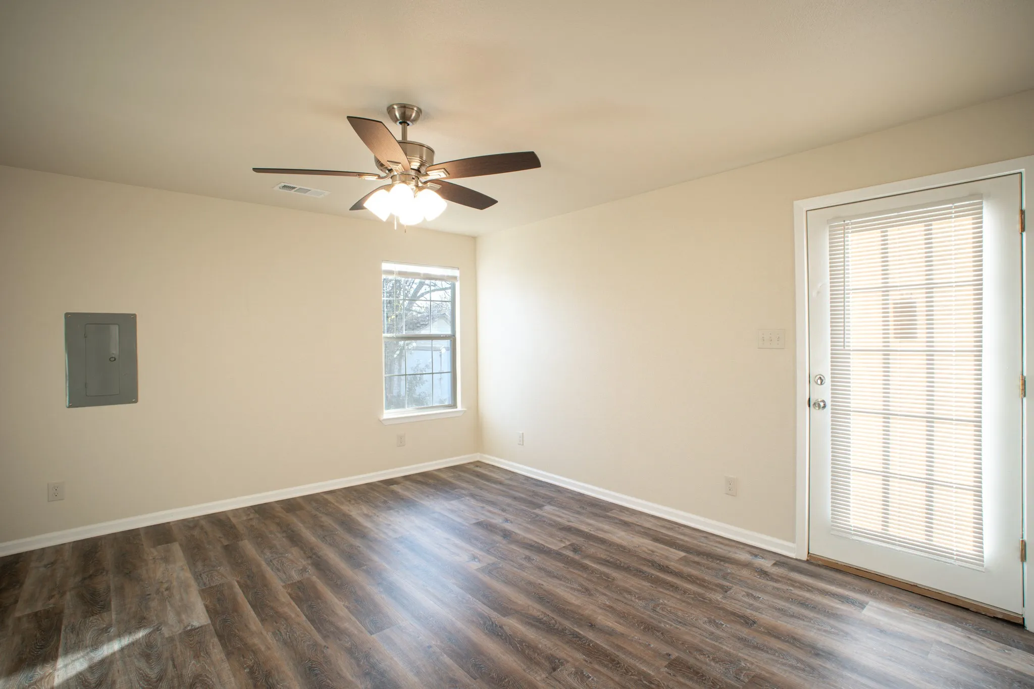 Spacious room featuring wood-finish flooring, light-colored walls, and a ceiling fan with integrated lighting