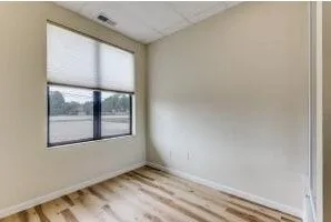Room featuring a large window with roller shades, light wood-finish flooring, and neutral wall paint