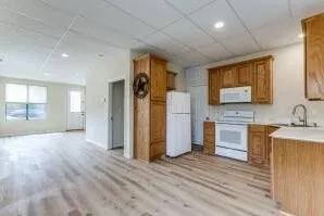 Kitchen featuring wood cabinetry, white appliances, and a stainless steel sink, with wood-finish flooring extending into an open living area