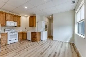 Kitchen area featuring wood-finish flooring, light wood cabinetry, white appliances, and a drop ceiling with recessed lighting