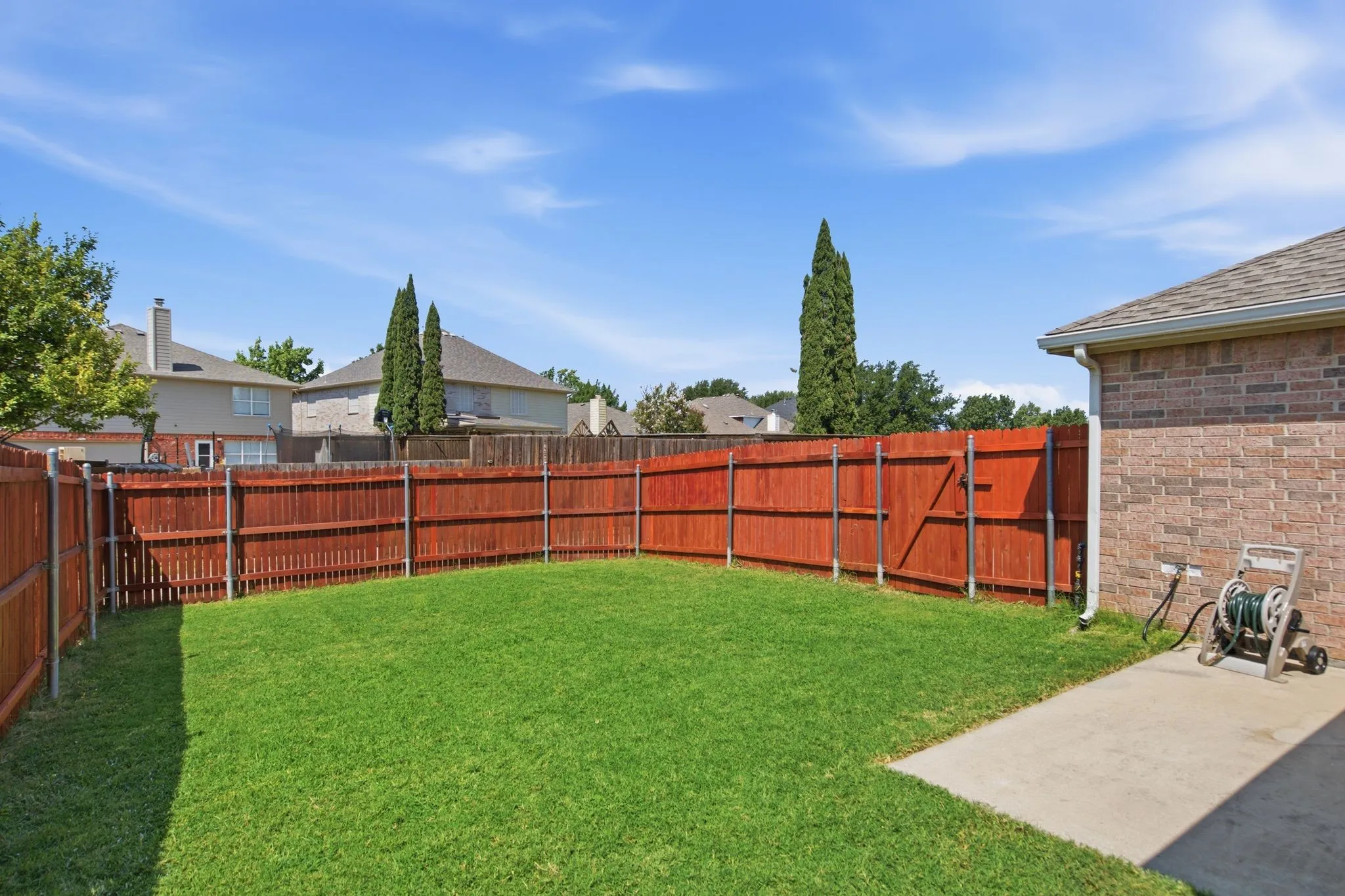 Expansive backyard featuring a lush lawn, privacy fencing, and a concrete patio