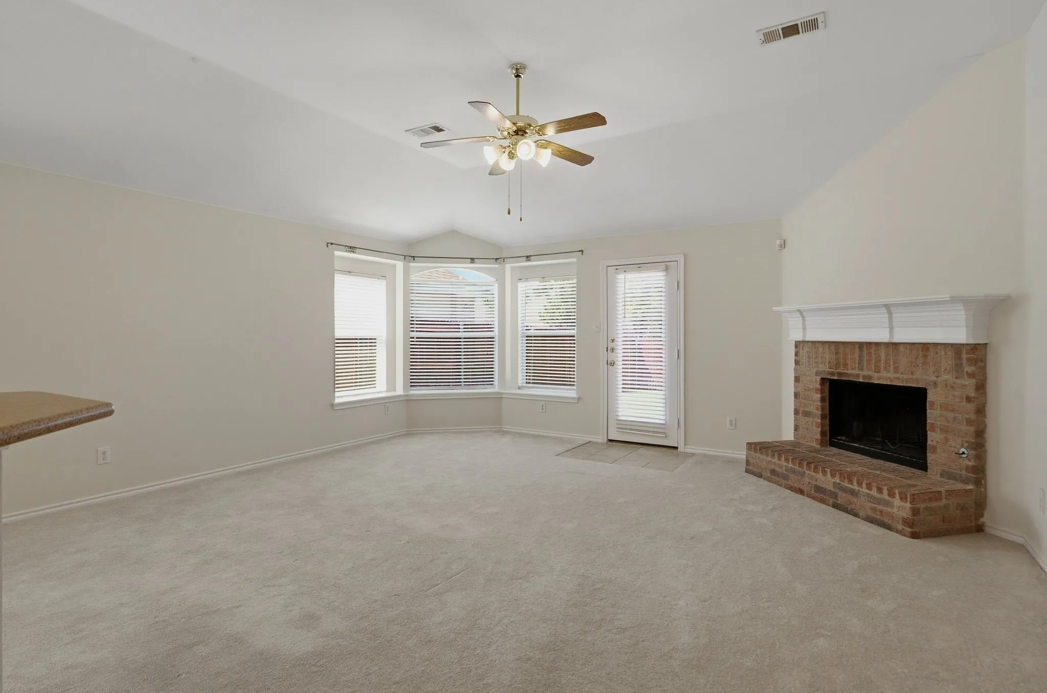 Living area featuring a brick fireplace with a white mantel, bay windows, and light-toned carpeting