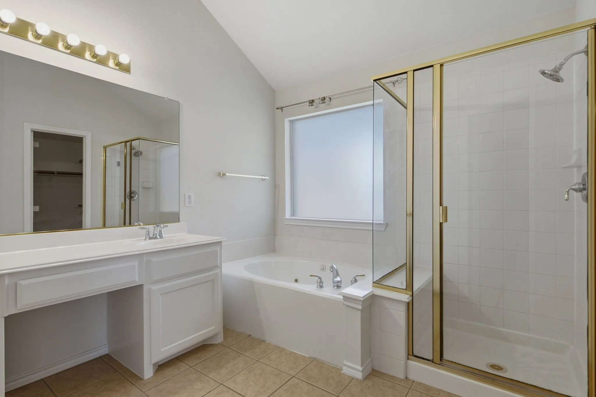 Primary Bathroom featuring a white vanity with integrated sink, a built-in jetted tub, a tiled shower with a gold-toned frame, and light-toned floor tile