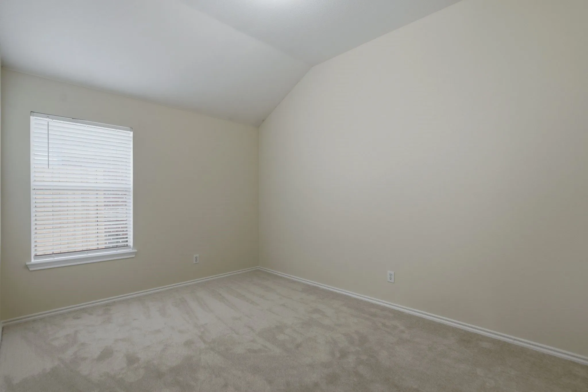 Room featuring plush neutral carpeting, vaulted ceiling, a window with horizontal blinds, and light-toned wall paint