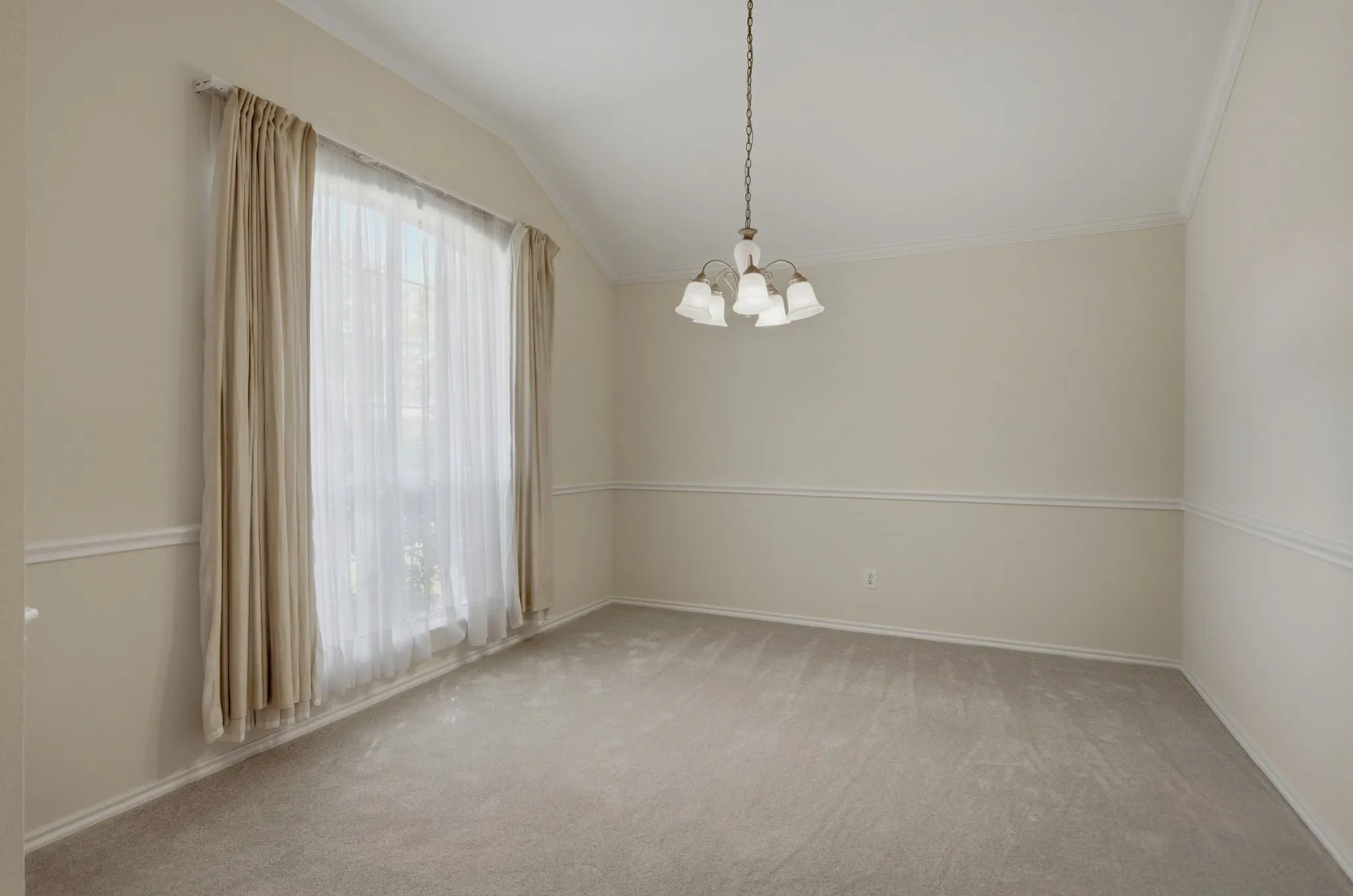 Spacious dining room featuring vaulted ceilings, a large window with sheers and drapes, and a traditional chandelier