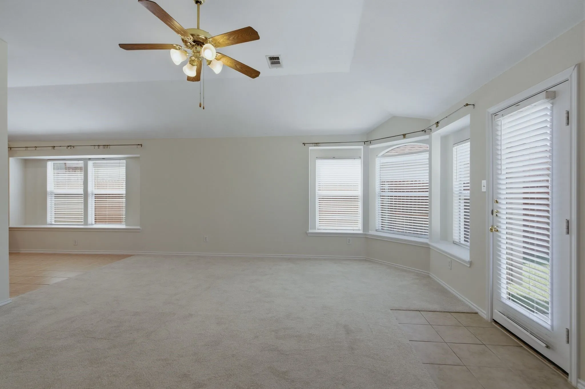 Spacious room featuring carpet flooring, multiple windows with blinds, a ceiling fan with light fixture, and a door with a full-length glass panel