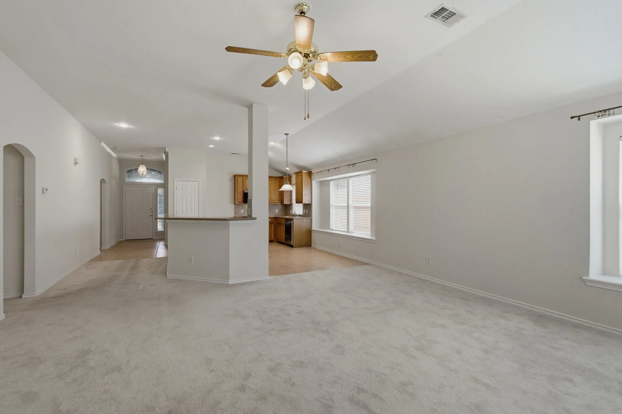 Spacious living area featuring light-toned carpeting, vaulted ceiling with a ceiling fan, and multiple windows