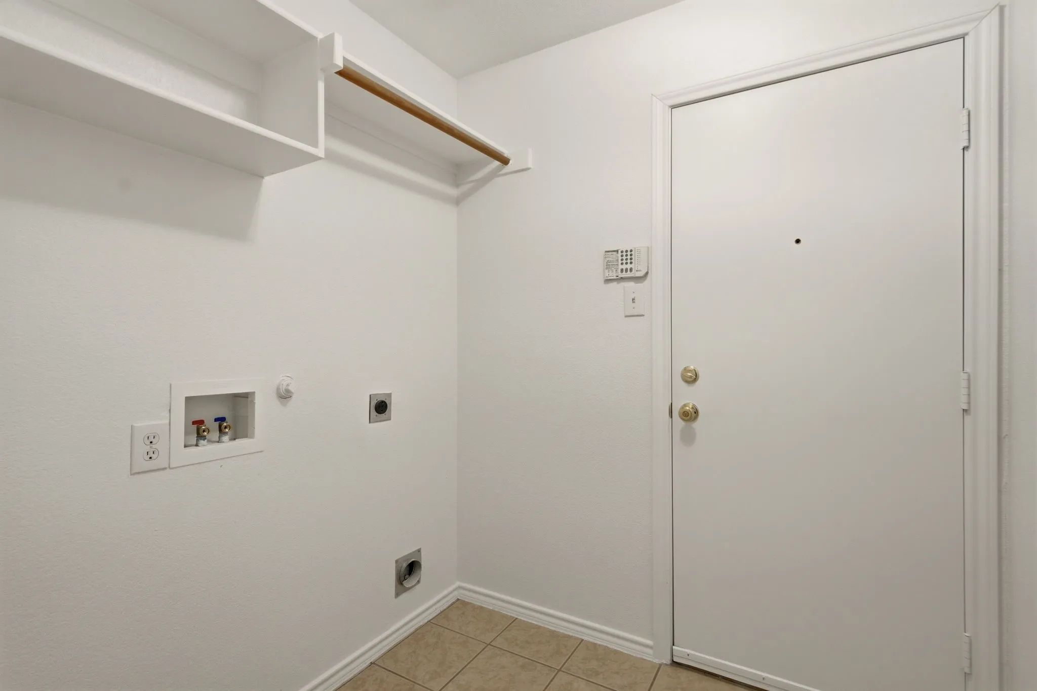 Utility area featuring white walls, tiled flooring, built-in shelving, and a clothing rod