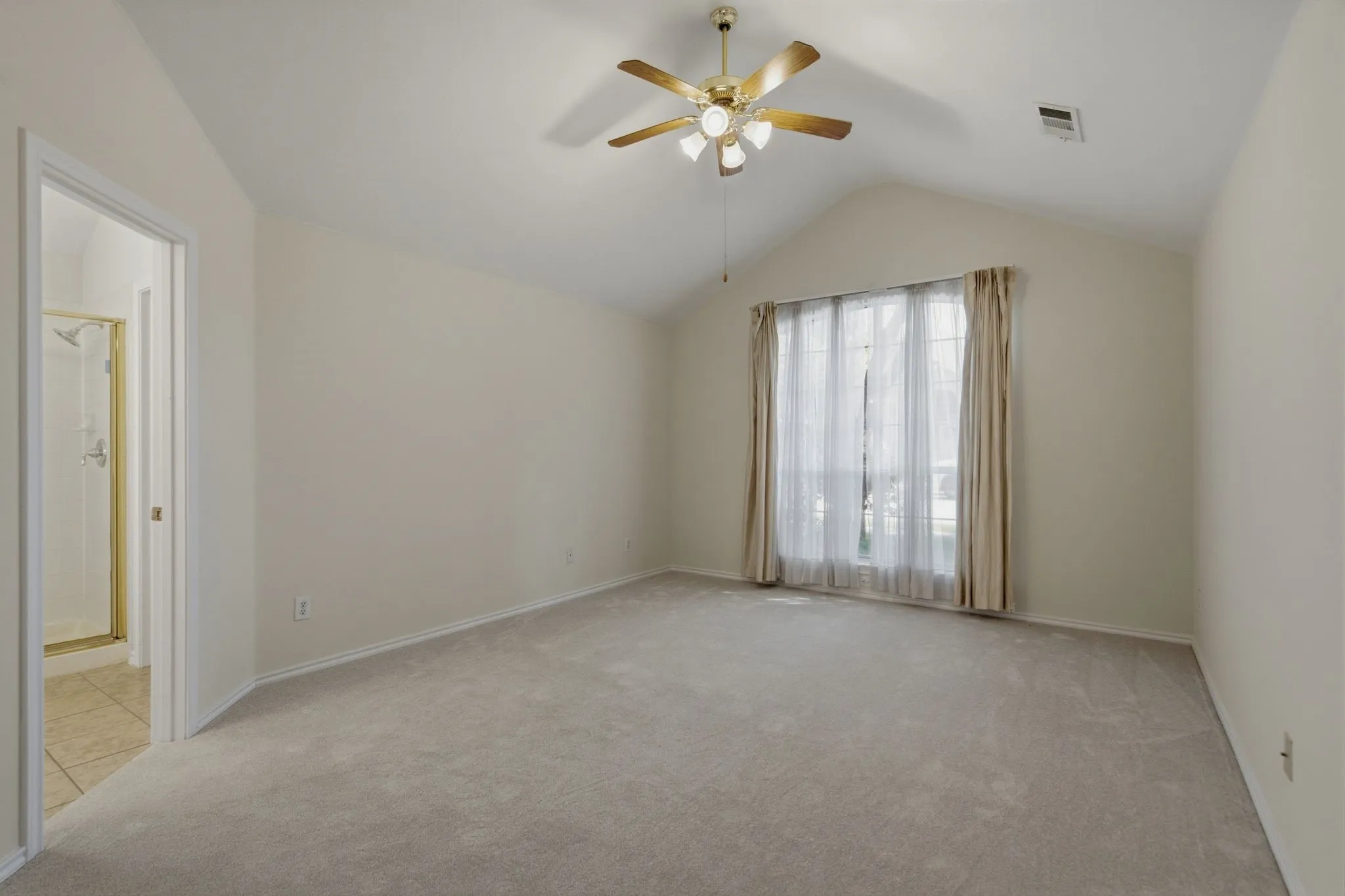 Primary bedroom featuring a vaulted ceiling with a brass-finish ceiling fan and a large window with drapes