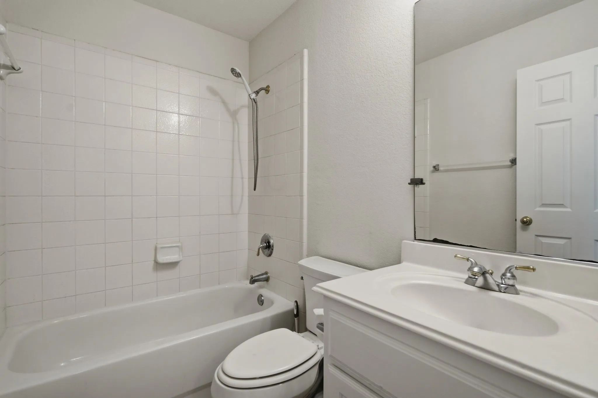 Bathroom featuring a white tiled shower/tub combination, a vanity with an integrated sink, a large wall-mounted mirror, and a white paneled door