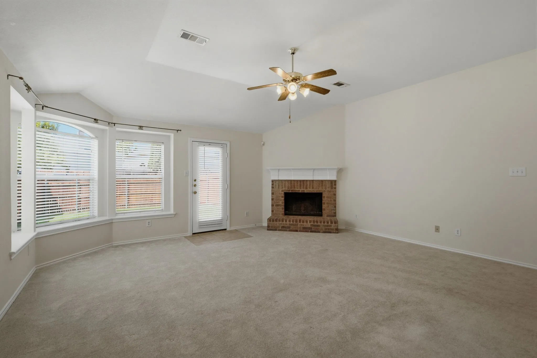 Spacious room featuring vaulted ceilings, a brick-surround fireplace with a white mantel, and a ceiling fan with integrated lighting