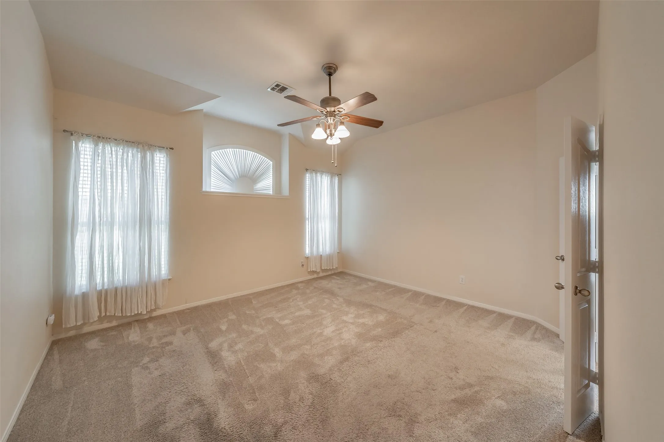 Spacious primary bedroom with vaulted ceiling, ceiling fan and multiple windows for natural light.