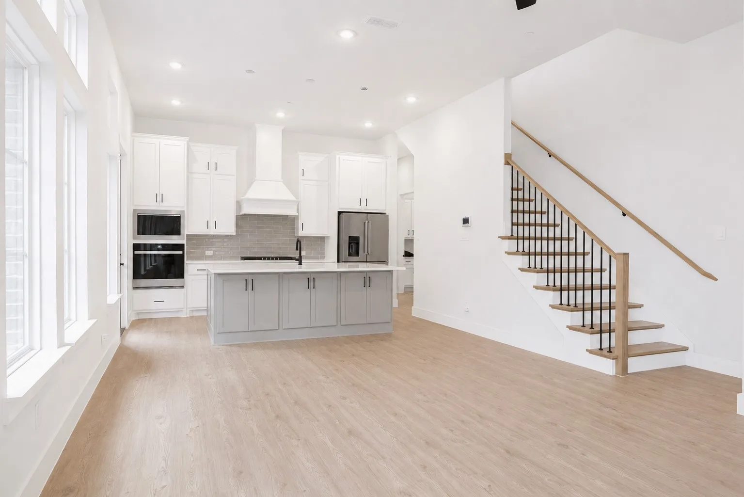 Open-concept kitchen with white cabinetry, a light gray island, stainless steel appliances, and wood-finish flooring