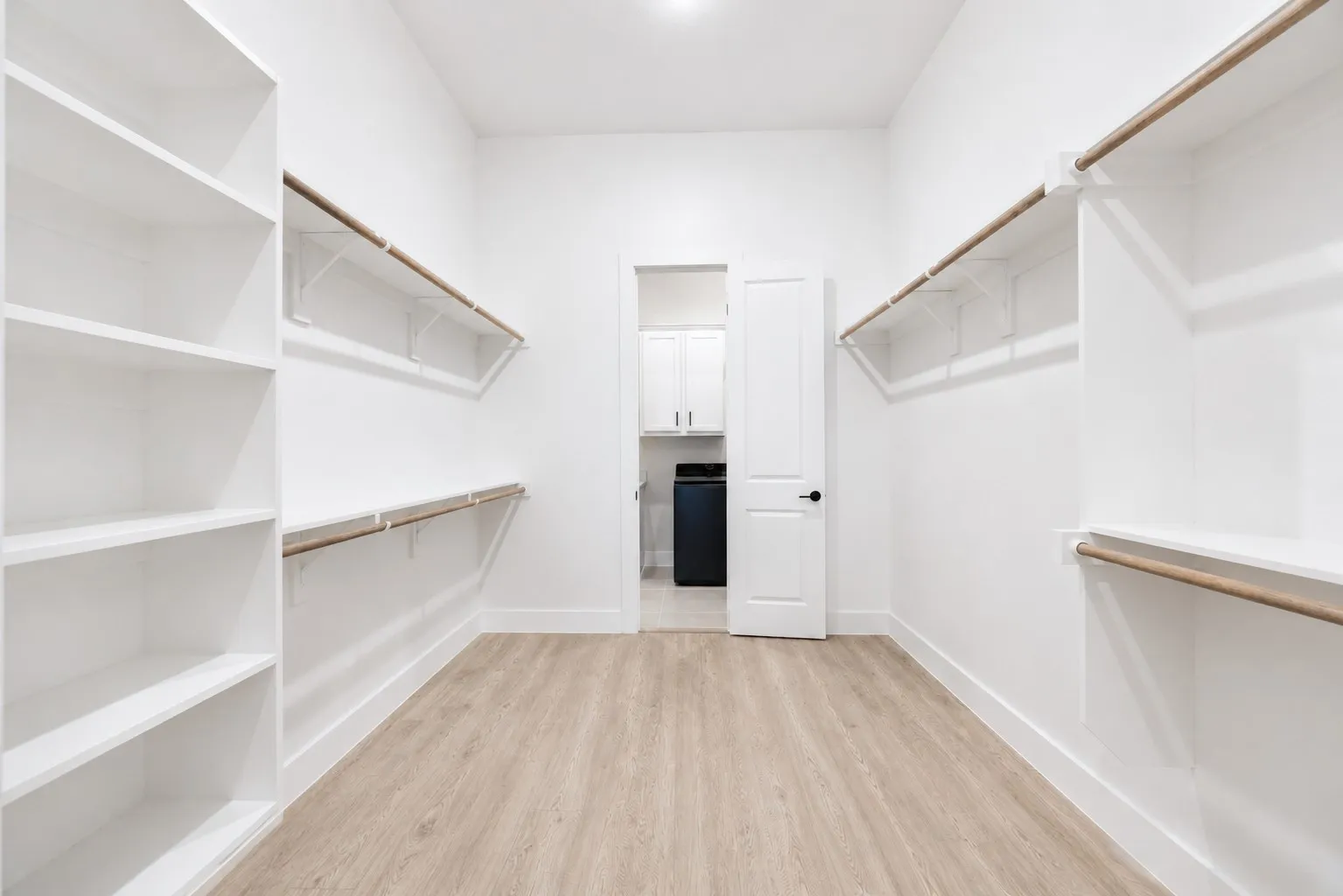 Spacious walk-in closet featuring light wood-finish flooring, white walls, and recessed lighting