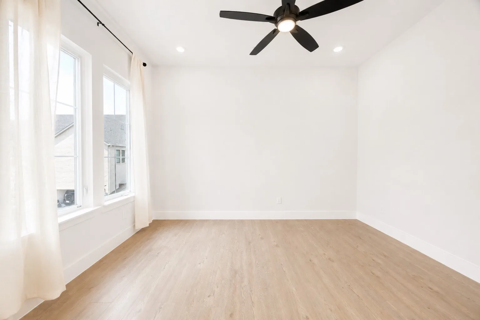 Bright room featuring light wood-finish flooring, white walls, and a black ceiling fan with integrated lighting