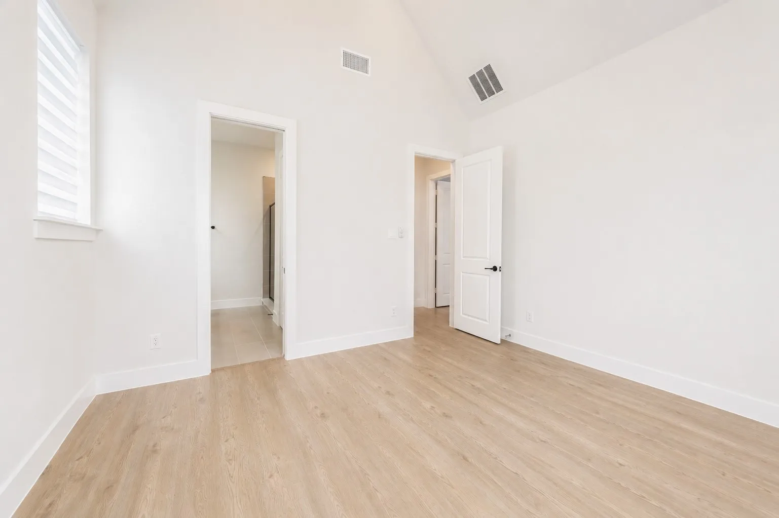 Room featuring vaulted ceilings, light wood-finish flooring, white walls, and a window with horizontal blinds