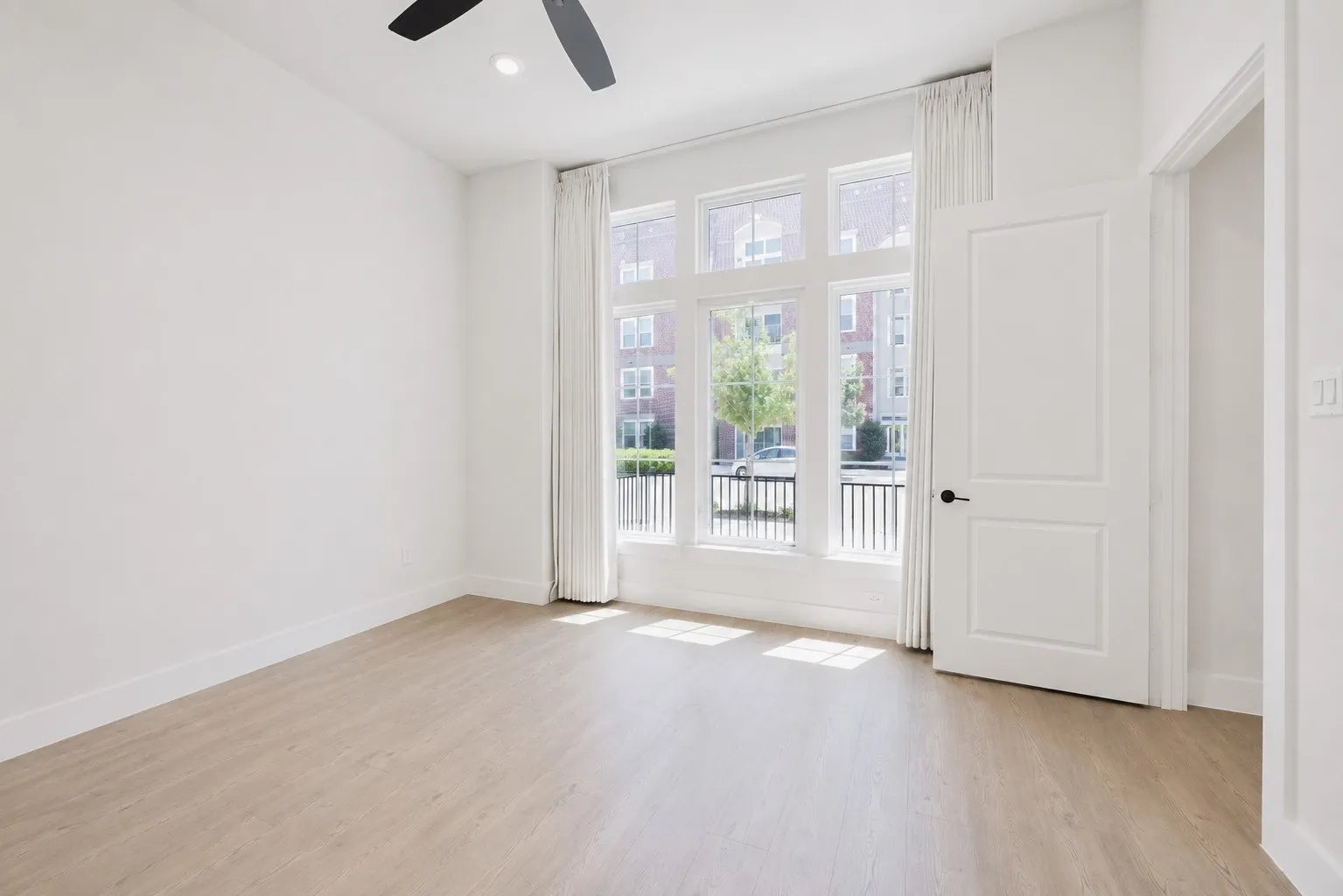 Bright room featuring large multi-pane windows, wood-finish flooring, a ceiling fan, and white trim
