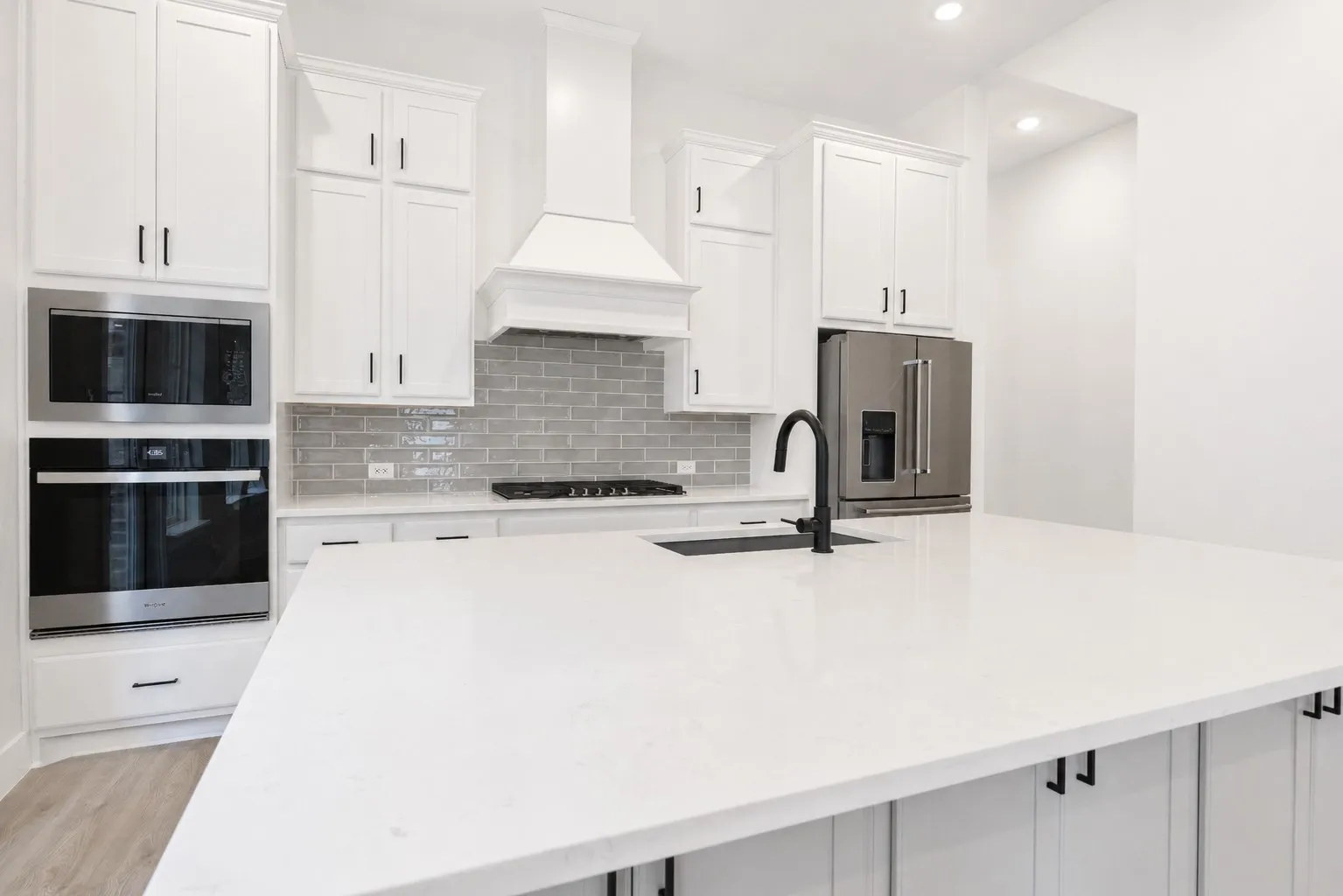 Kitchen featuring an expansive island with a matte black faucet, white shaker cabinetry, stainless steel appliances, and a gray subway tile backsplash