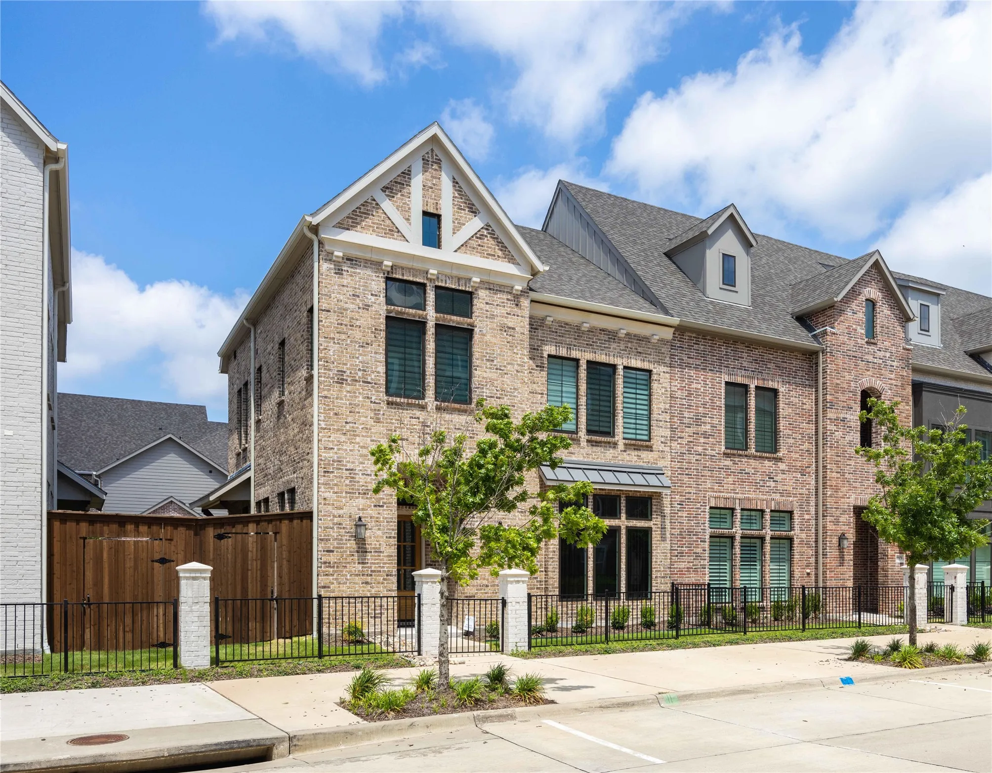 Contemporary townhome featuring a brick facade with stone accents, a gabled roofline, dormer windows, and a black wrought iron fence