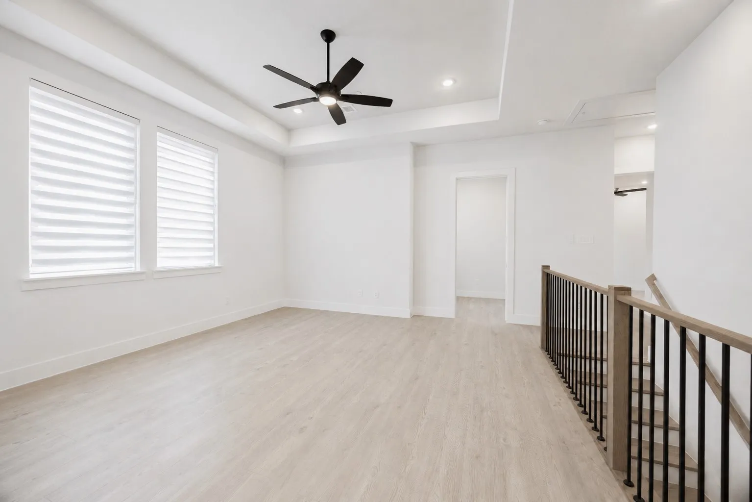 Spacious upper-level room featuring wood-finish flooring, two large windows with blinds, a modern ceiling fan, and recessed lighting