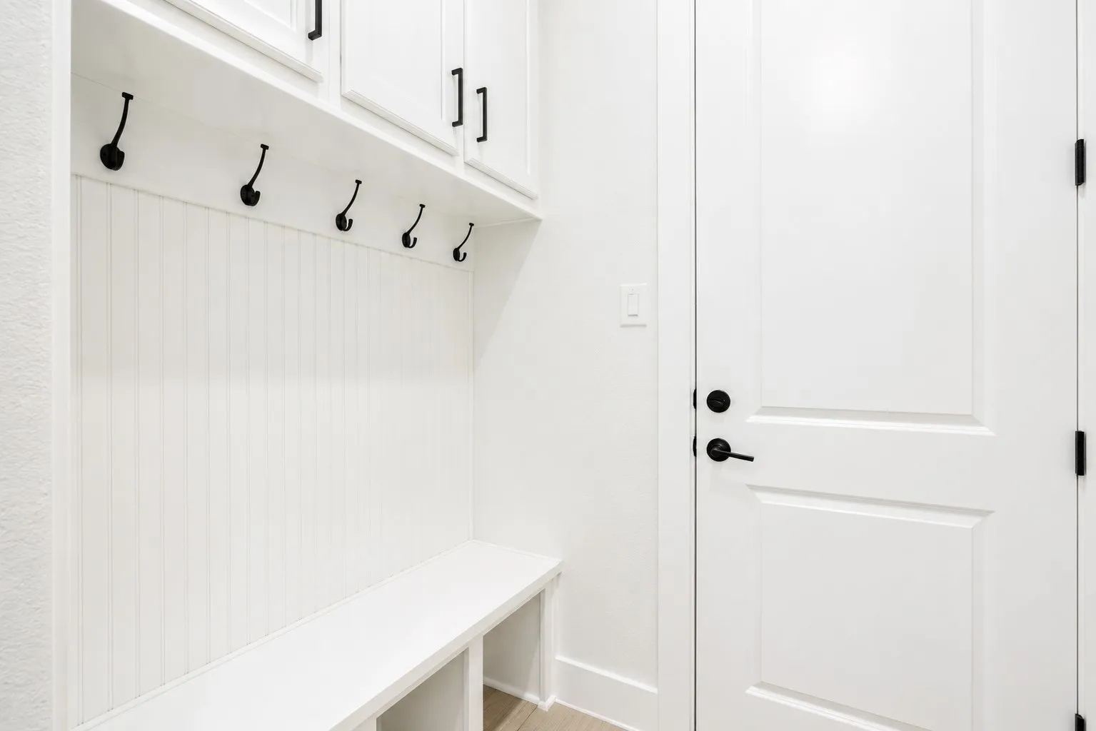 Built-in mudroom bench with beadboard backing, overhead cabinetry, and black hardware