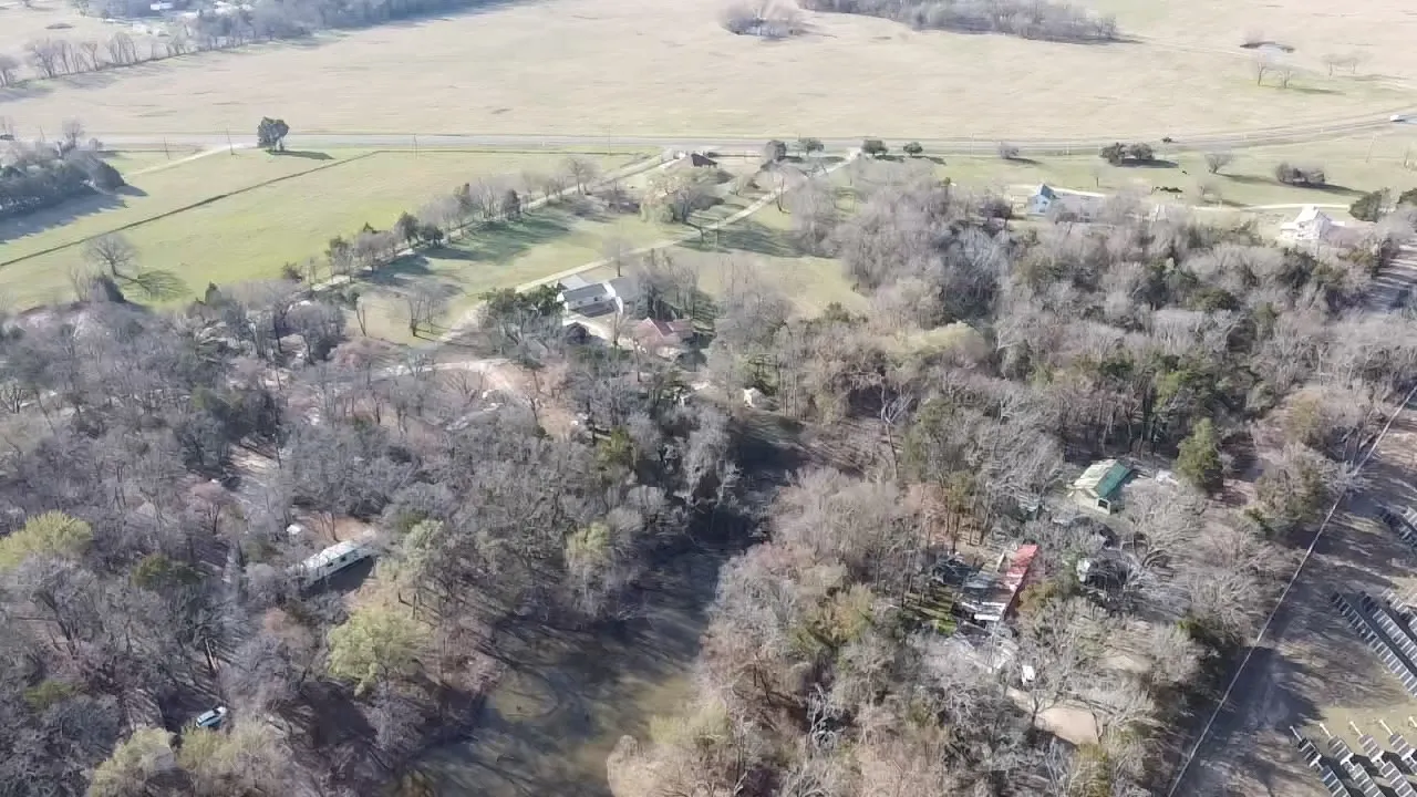 Expansive property featuring wooded areas, open fields, and scattered residential structures