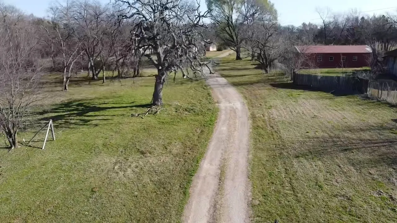 Expansive grounds featuring a meandering dirt road, mature trees, and a red outbuilding