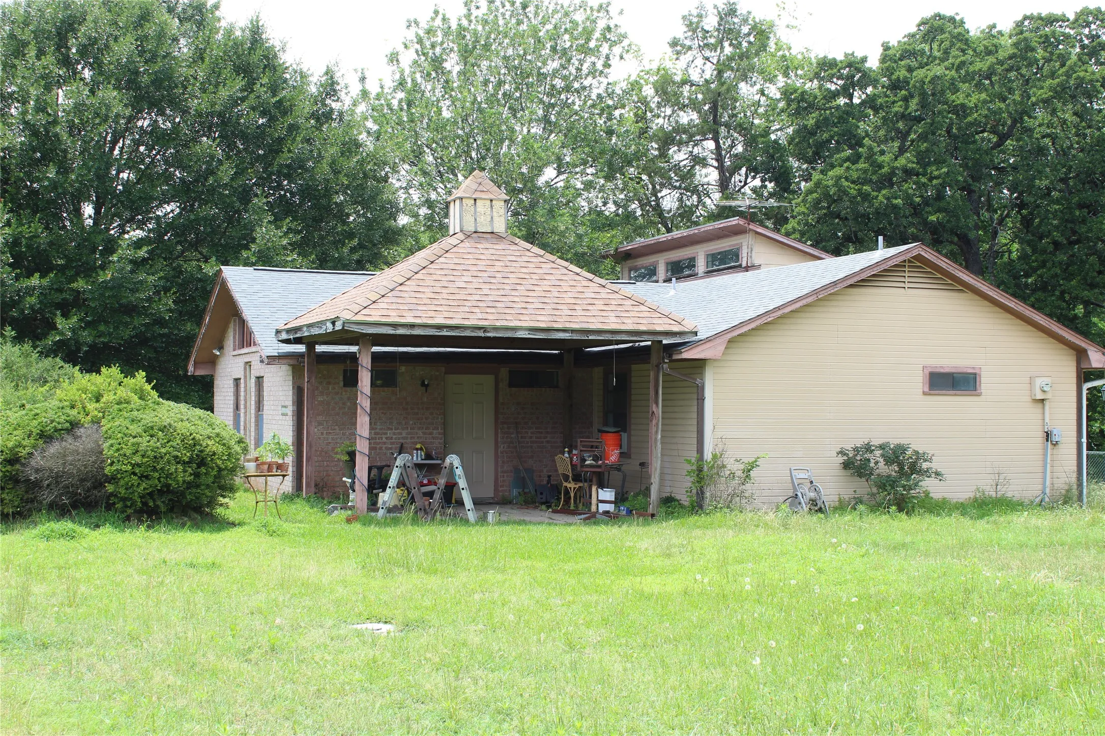 Rear exterior featuring a covered patio with a cupola roof, a dormer with multiple windows, and a brick facade