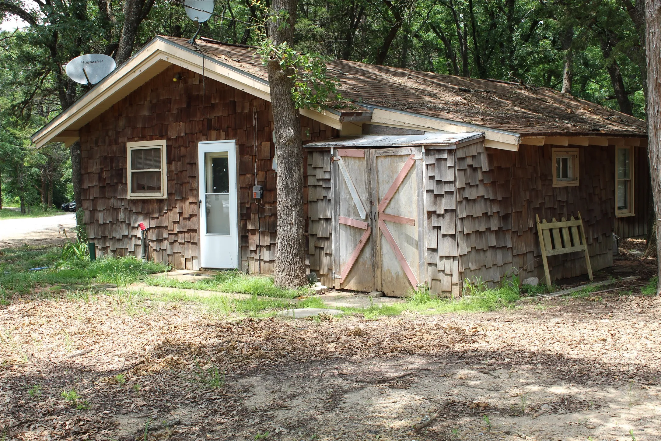 Wood shingle exterior with gable roofline and a visible storage shed featuring double doors