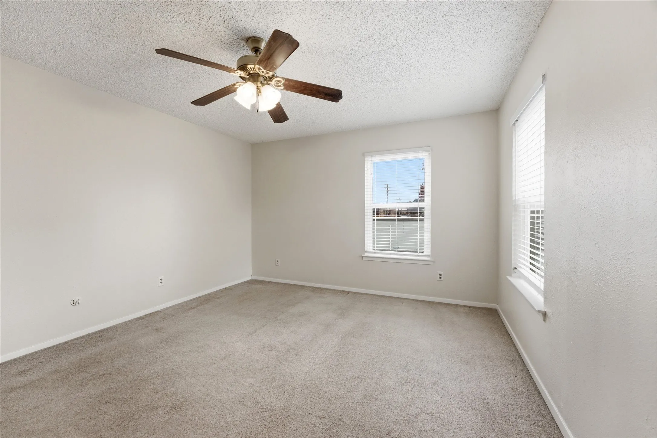 Spacious room featuring neutral carpeting, light-toned walls, and multiple windows with blinds