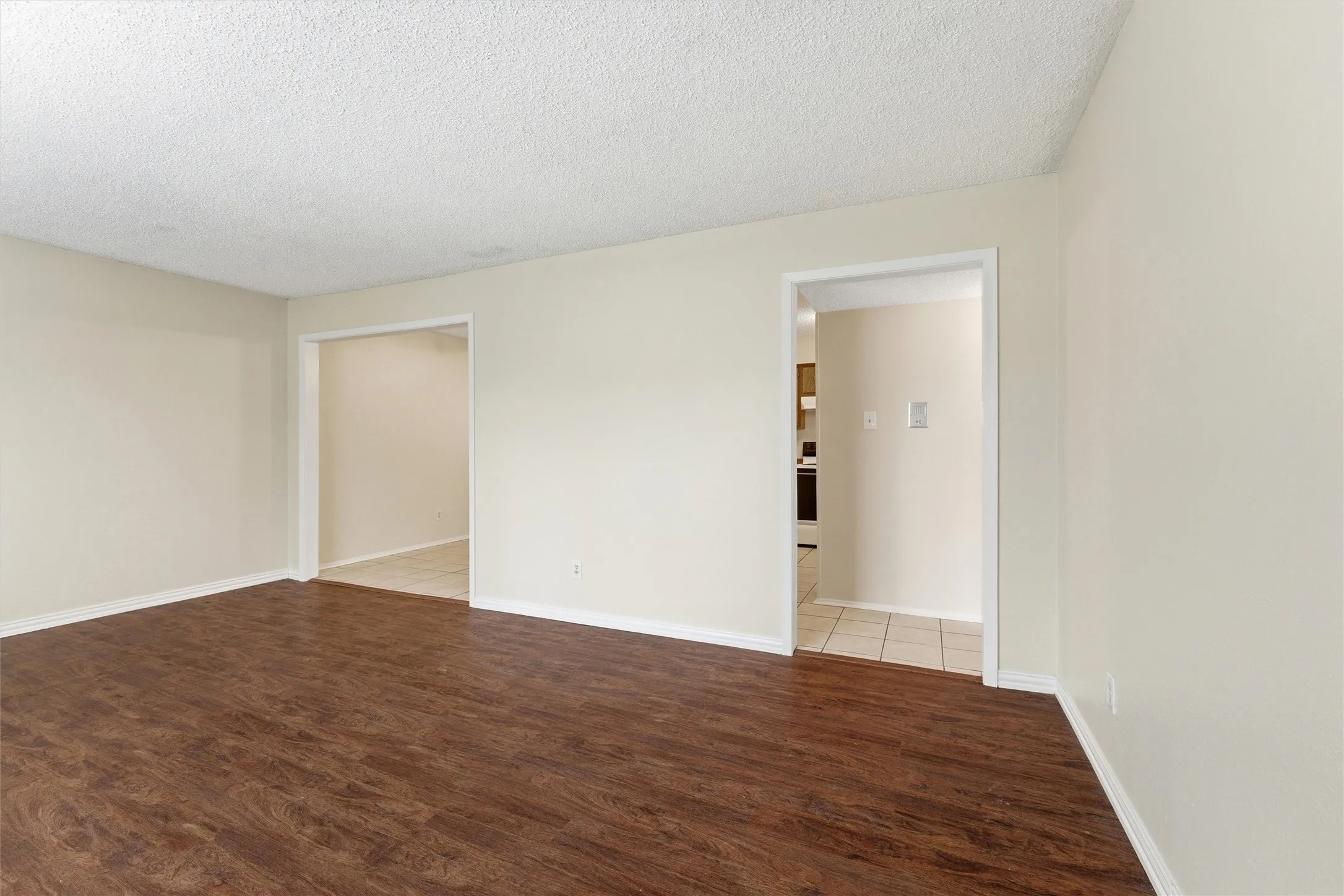 Spacious interior featuring wood-finish flooring, light neutral wall tones, white trim, and two open doorways