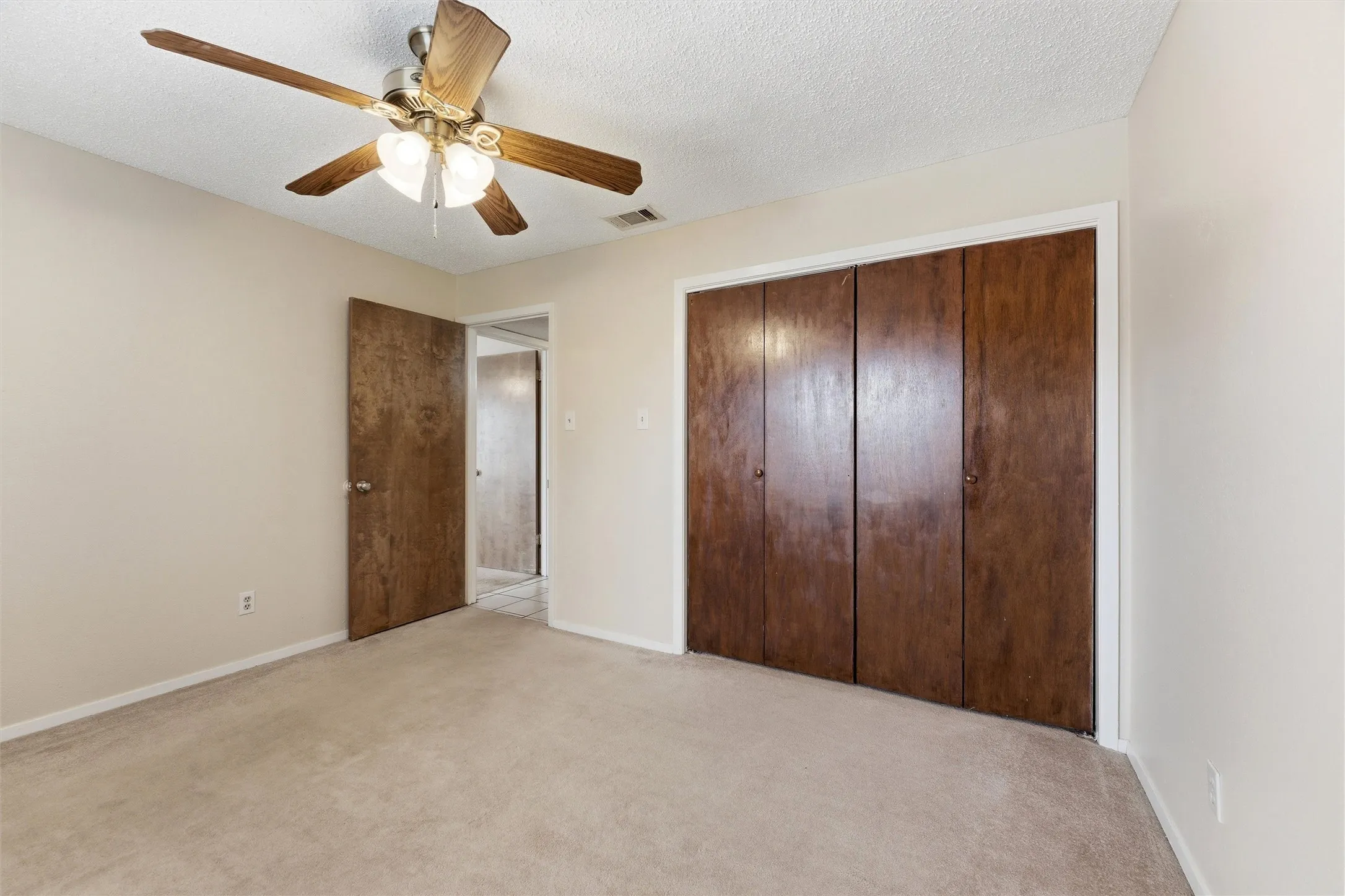 Carpeted room featuring a ceiling fan with integrated lighting, wood-finish bi-fold closet doors, and light-toned walls