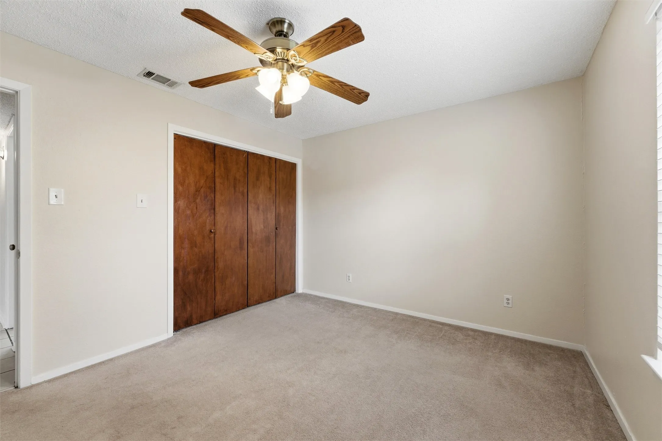 Neutral wall paint, plush carpet flooring, a ceiling fan with integrated lighting, and bi-fold closet doors