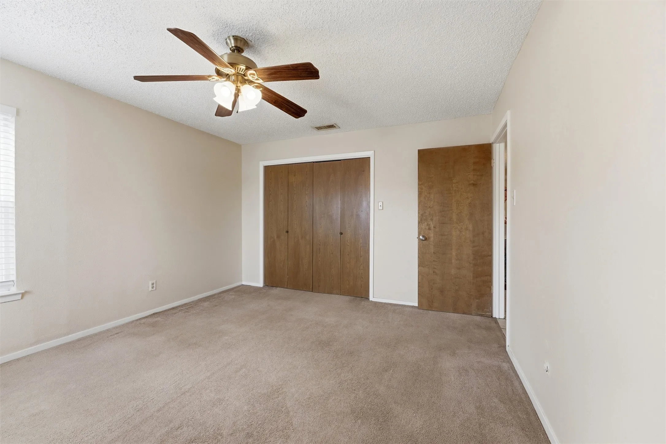 Spacious room featuring neutral carpeting, light-toned walls, and a ceiling fan with integrated lighting