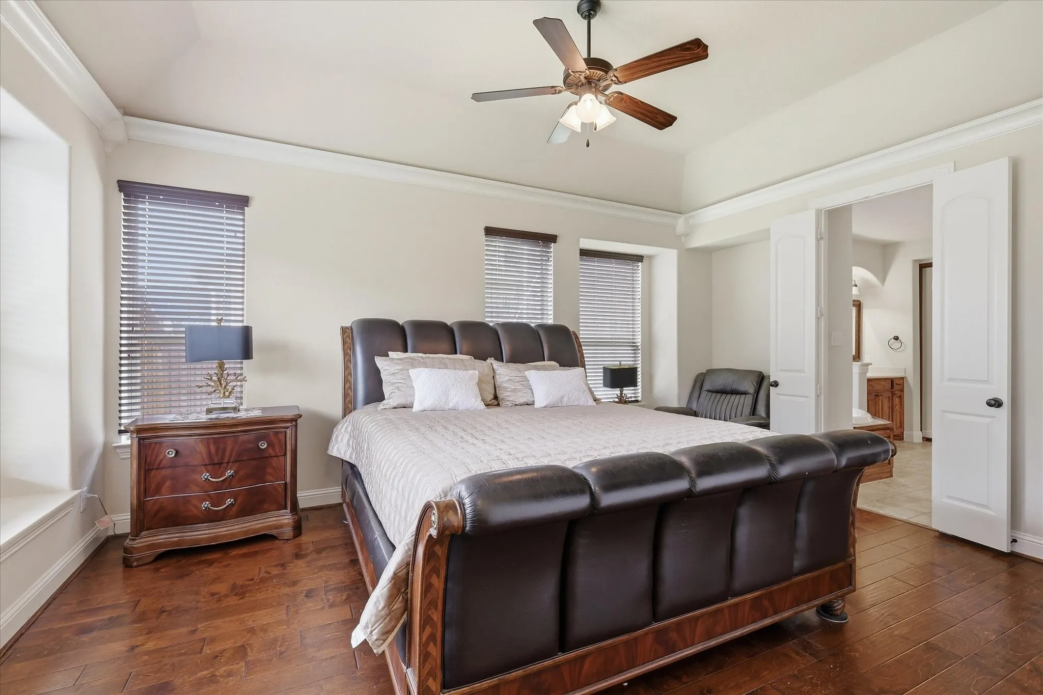 Spacious primary retreat featuring rich hardwood flooring, a ceiling fan, and an abundance of natural light from multiple windows. The room easily accommodates a large bed and sitting area, while an adjoining flex space offers flexibility for a home office or reading nook. A warm, elegant design creates a comfortable and private escape at the end of the day.