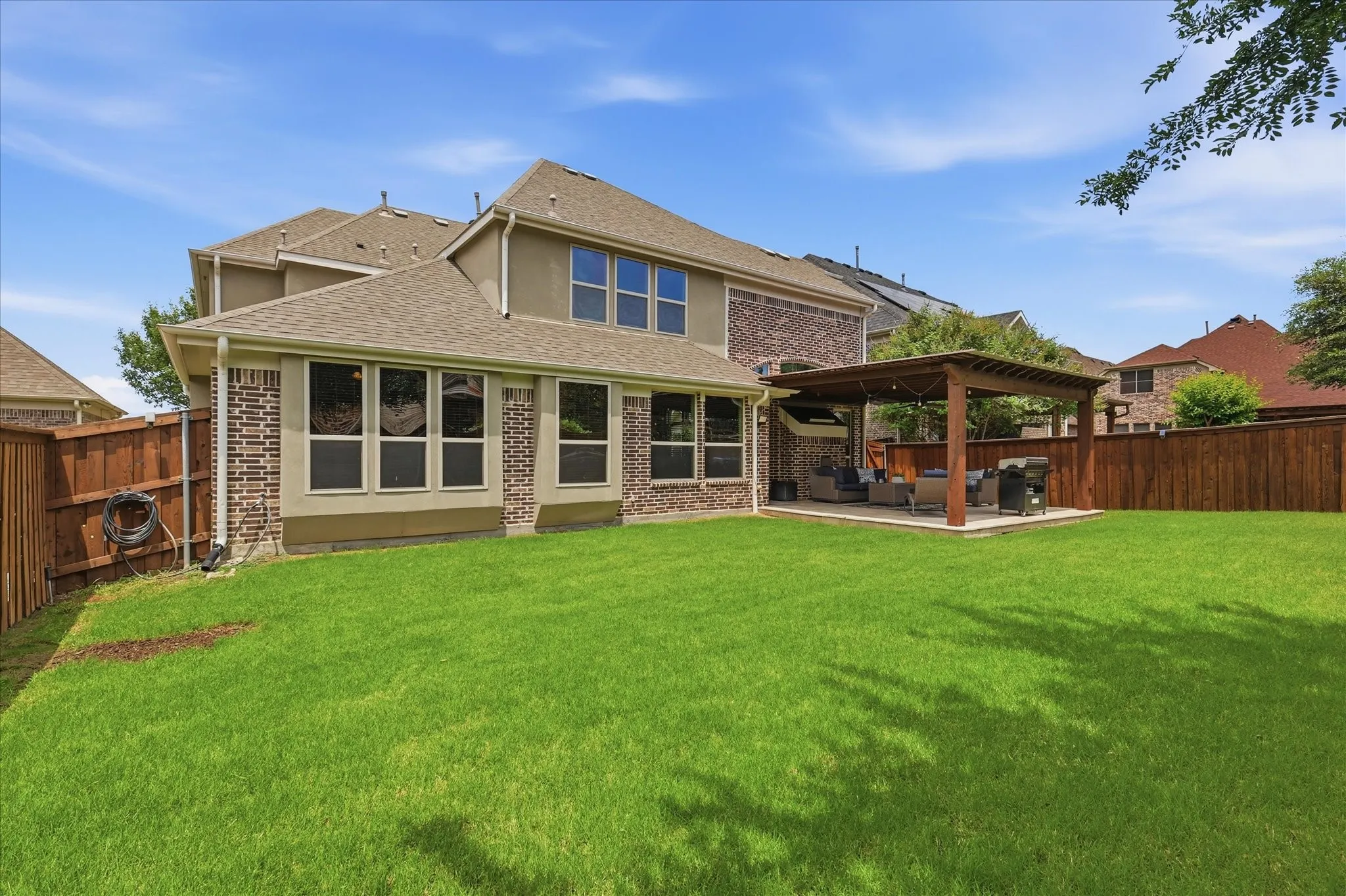 Beautifully maintained backyard featuring a large, lush lawn perfect for outdoor activities and privacy fencing on all sides. The covered pergola patio offers a shaded seating area, ideal for relaxing or entertaining. Numerous windows across the back of the home bring in abundant natural light, seamlessly connecting the indoor and outdoor living spaces.