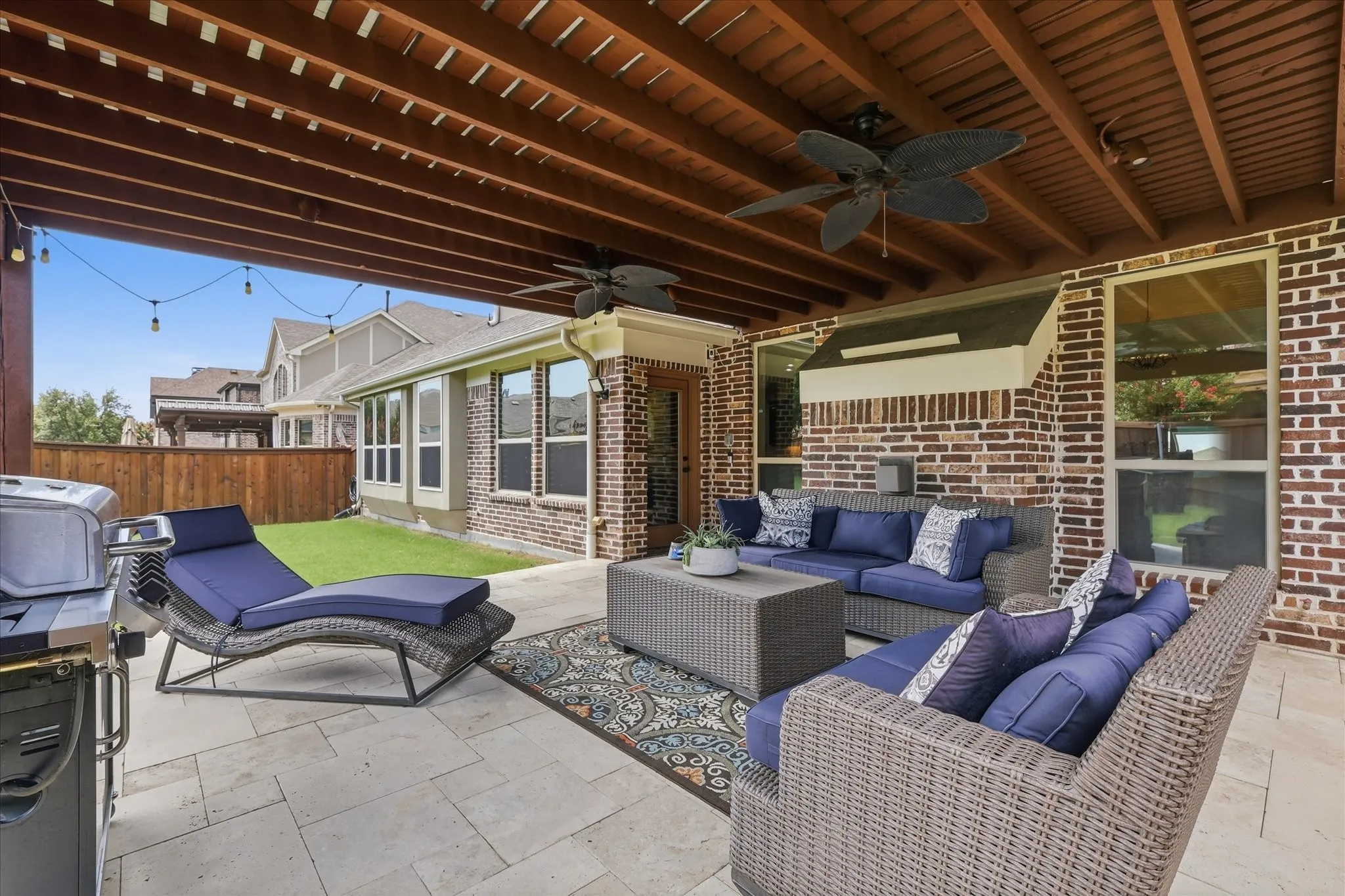 A stone-paved surface anchors the large outdoor space overlooking a fenced backyard with mature trees and lush green lawn for added privacy.