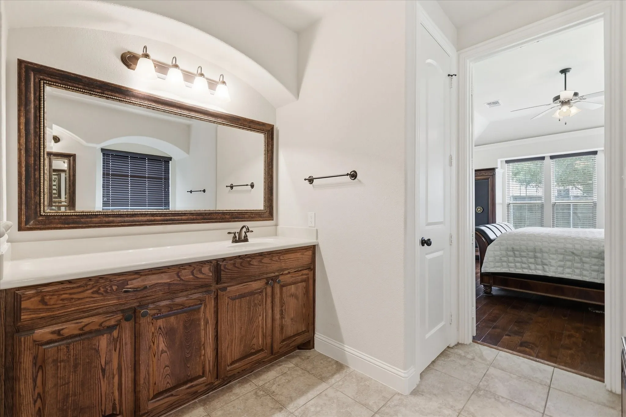 A dark wood vanity offers plenty of storage beneath a wide countertop with dual sinks, framed by a large mirror and elegant vanity lighting.