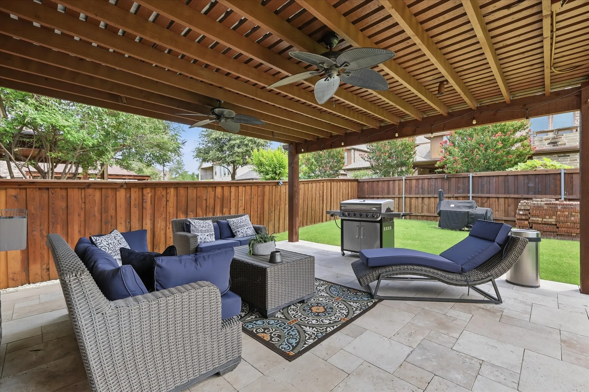 Expansive covered patio designed for outdoor living and entertaining, featuring a wood pergola ceiling with dual fans for added comfort.