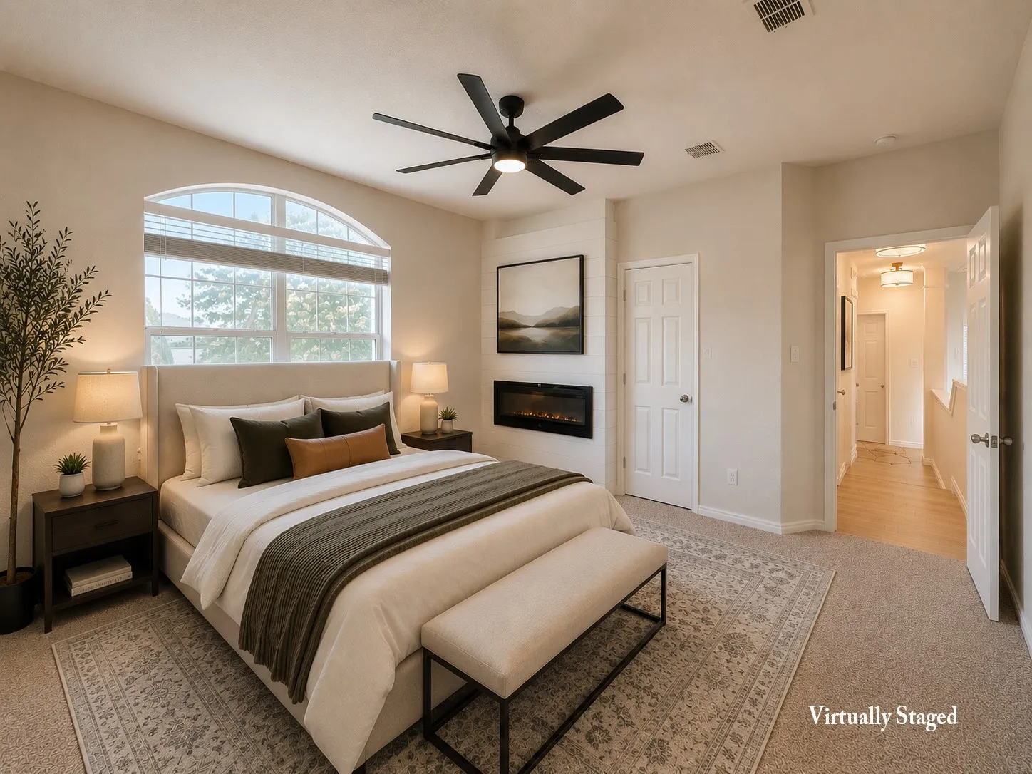 Carpeted bedroom with a large arched window, featuring a ceiling fan, built-in fireplace, and a five-panel door