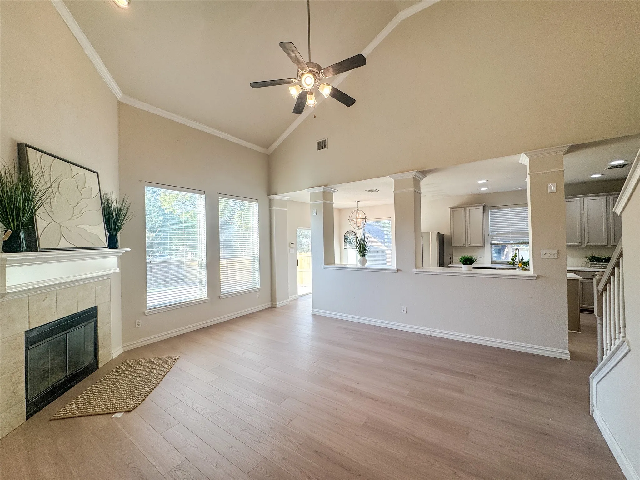 Vaulted ceiling featuring a ceiling fan, light wood-finish flooring, a tile-surround fireplace with a white mantel, and multiple windows