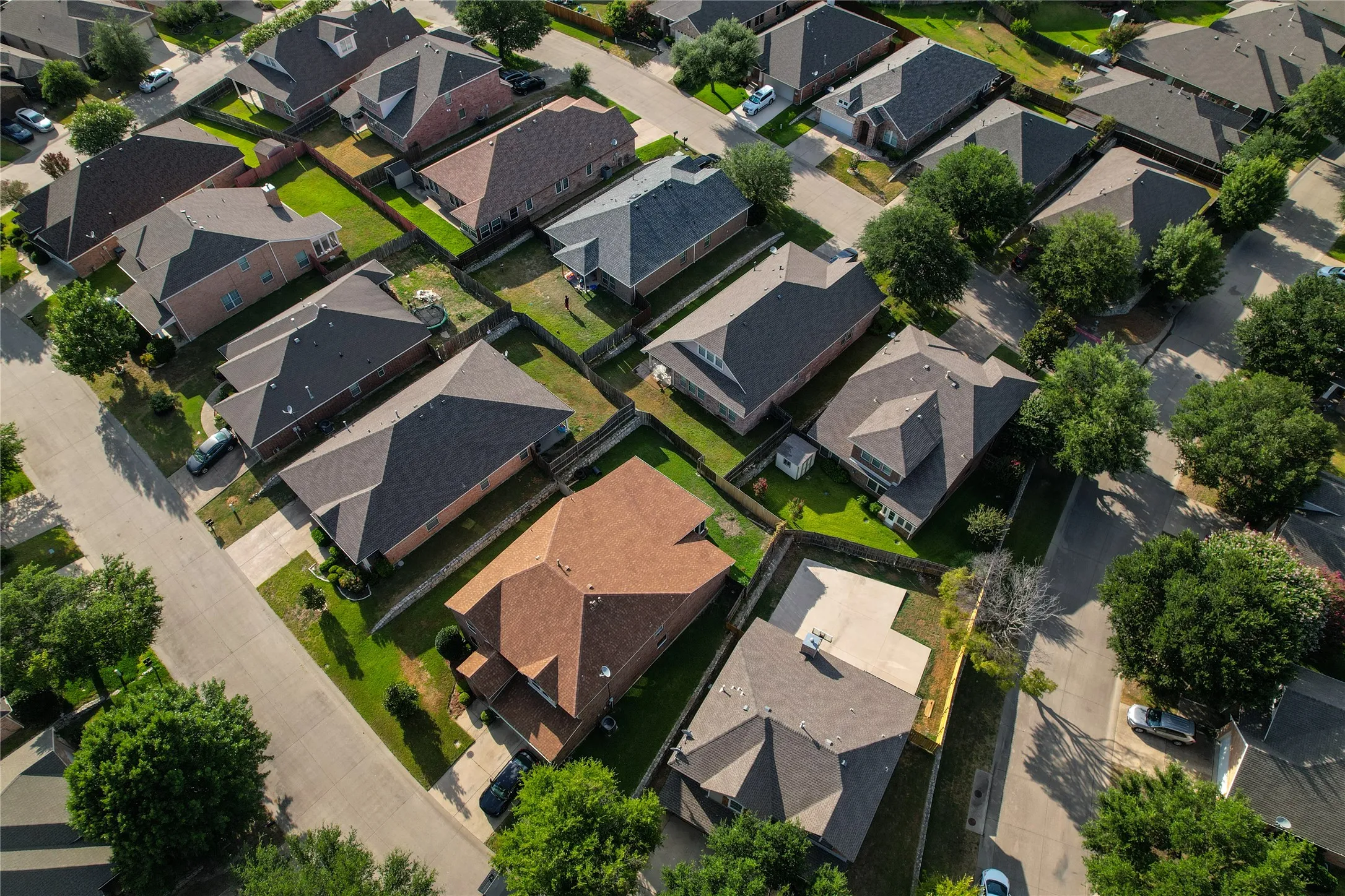 Aerial perspective of a residential neighborhood featuring asphalt streets, mature trees, and varied architectural styles with shingle roofs