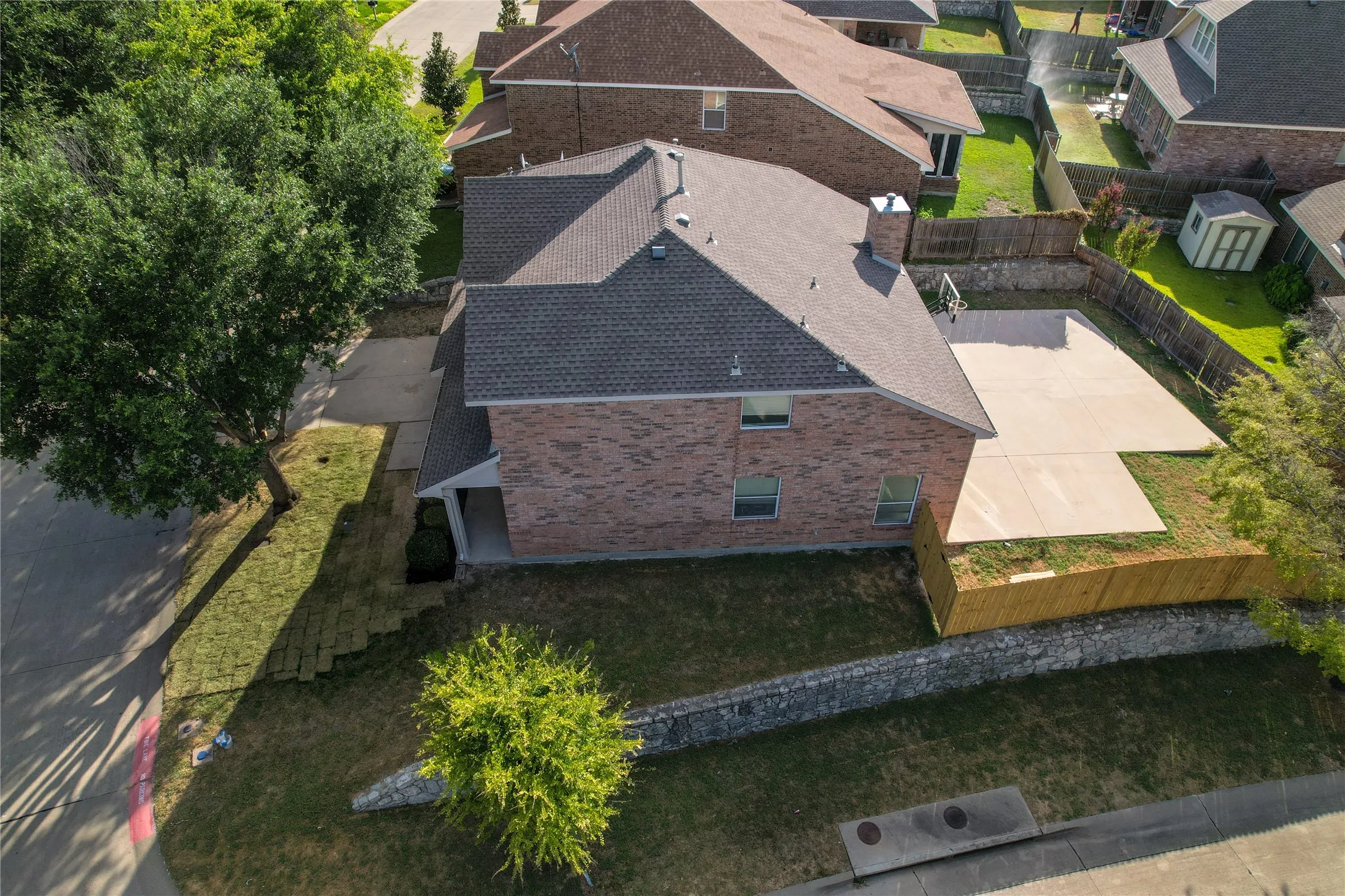 Brick exterior home featuring a composition shingle roof, mature front yard tree, concrete driveway, and a spacious concrete patio in the rear yard