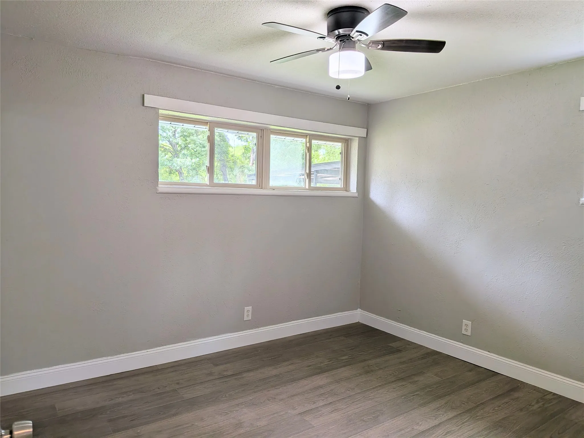 Room featuring wood-finish flooring, a multi-pane window, white baseboards, and a ceiling fan with integrated lighting