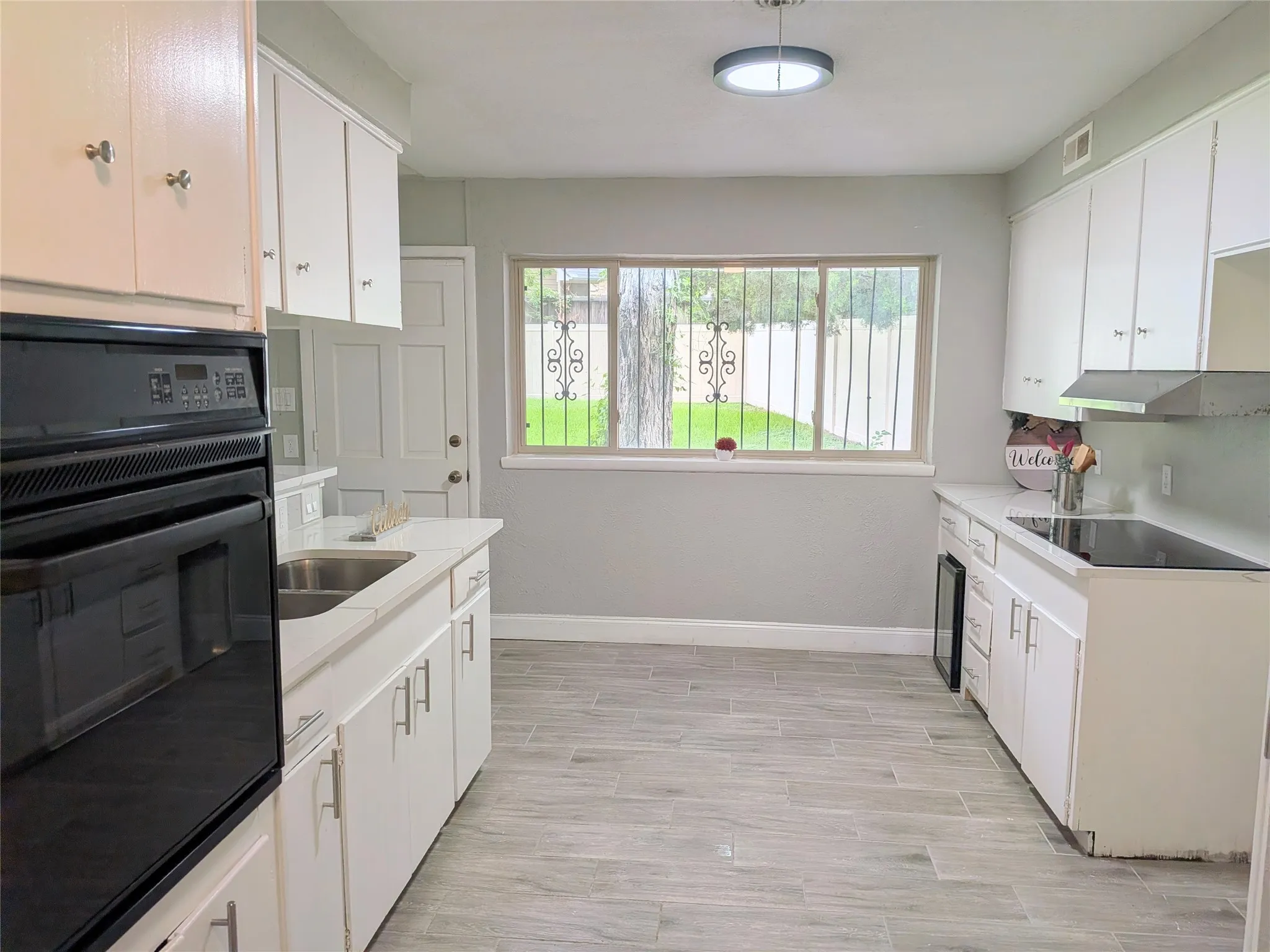 Kitchen featuring light wood-finish flooring, white cabinetry with silver-tone hardware, a built-in oven, and a built-in stovetop